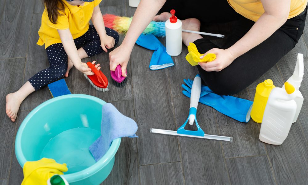 A beautiful young woman and her little daughter are cleaning the floor with brushes in the kitchen.