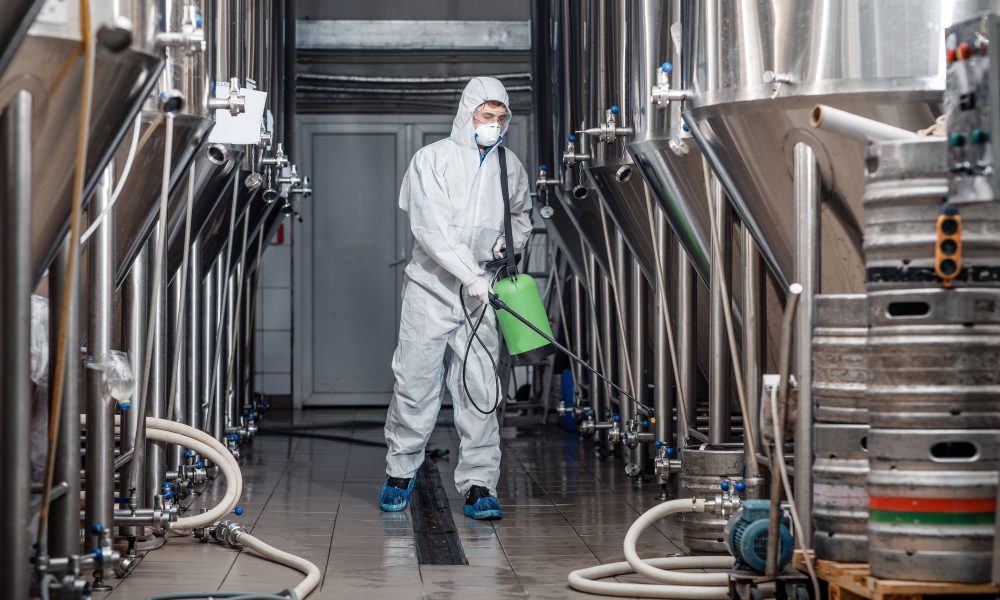 Factory cleaning. Man in protective suit and mask disinfects plant