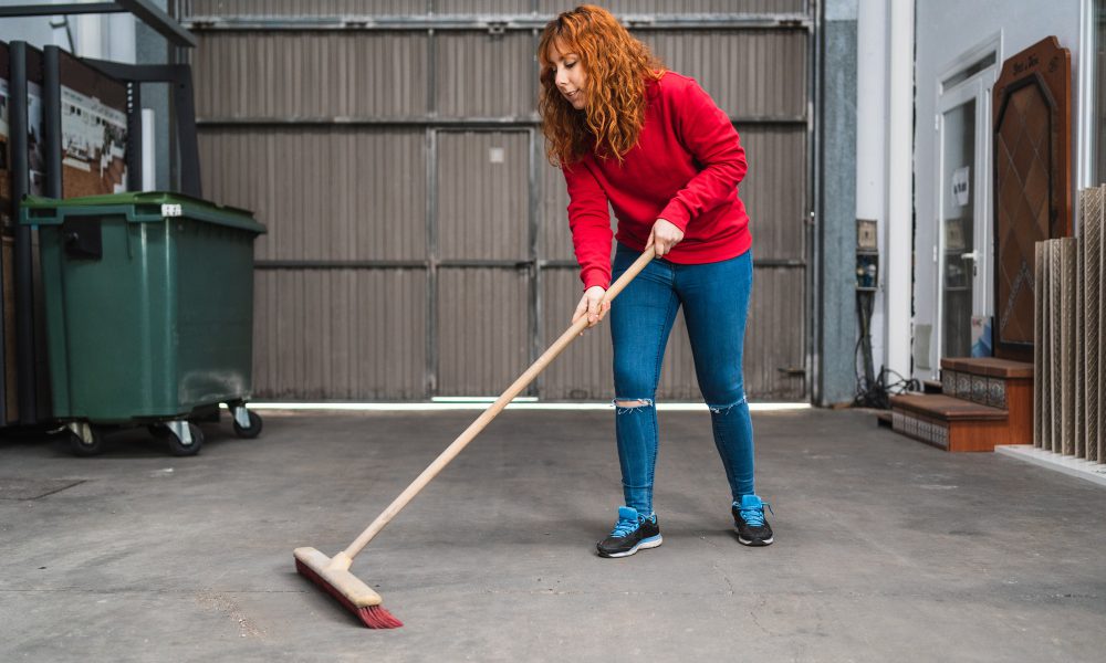 Female worker sweeping the garage with a large broom