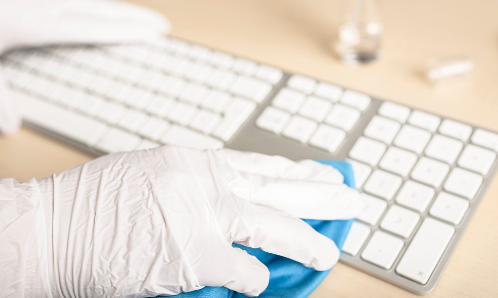 Hand with gloves cleaning a keyboard with disinfectant