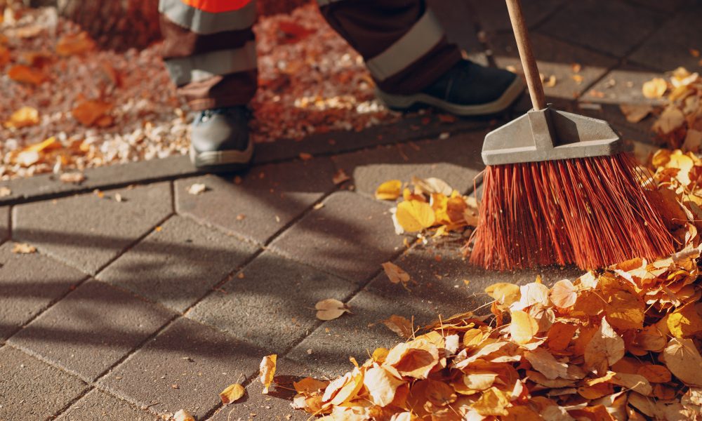 Janitor cleaner sweeping autumn leaves on the street