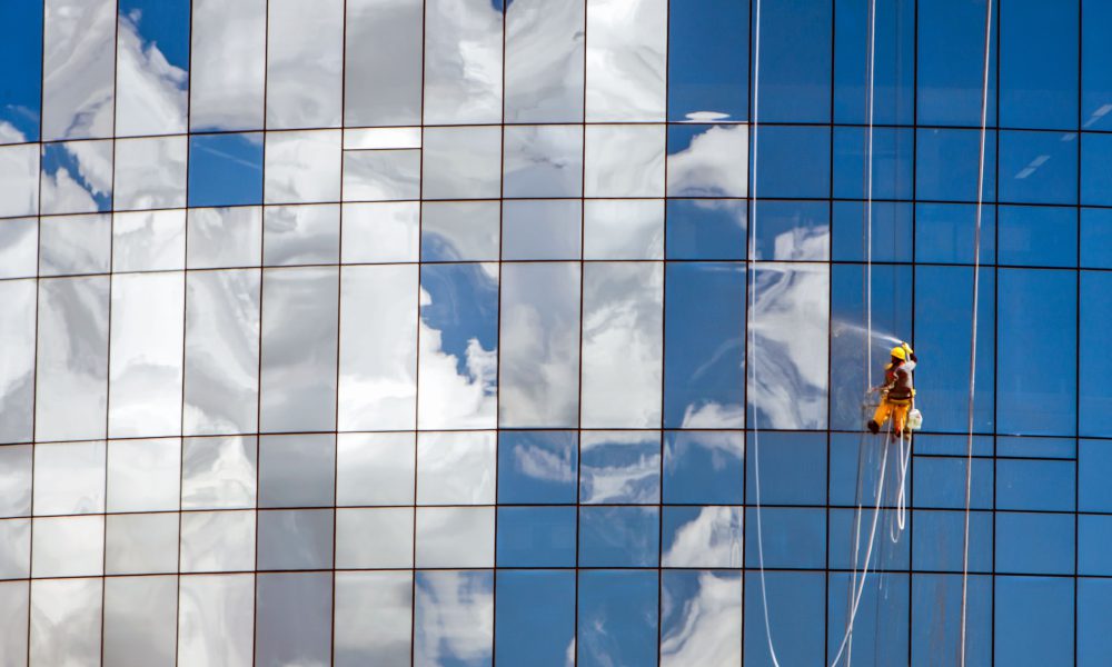 Worker cleaning glass windows of modern building